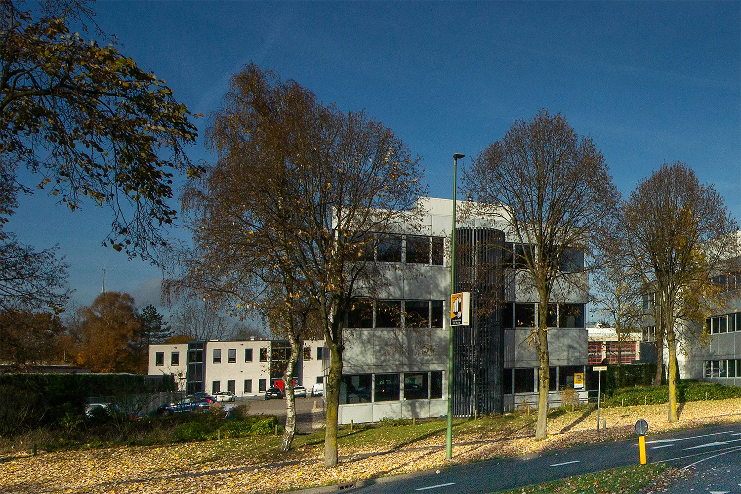 Kantoorpand aan de Huis-ter-Heideweg omringd door bomen op een zonnige herfstdag.